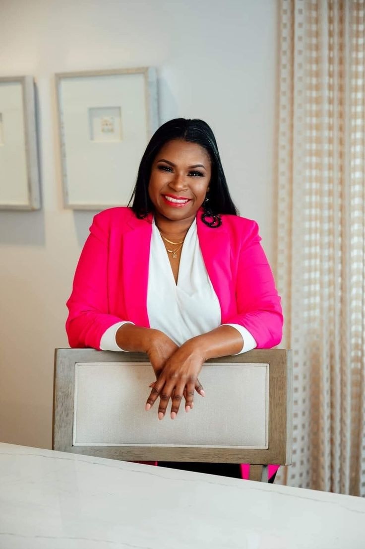 Josette — hot pink blazer, white blouse, leaning on chair, office setting