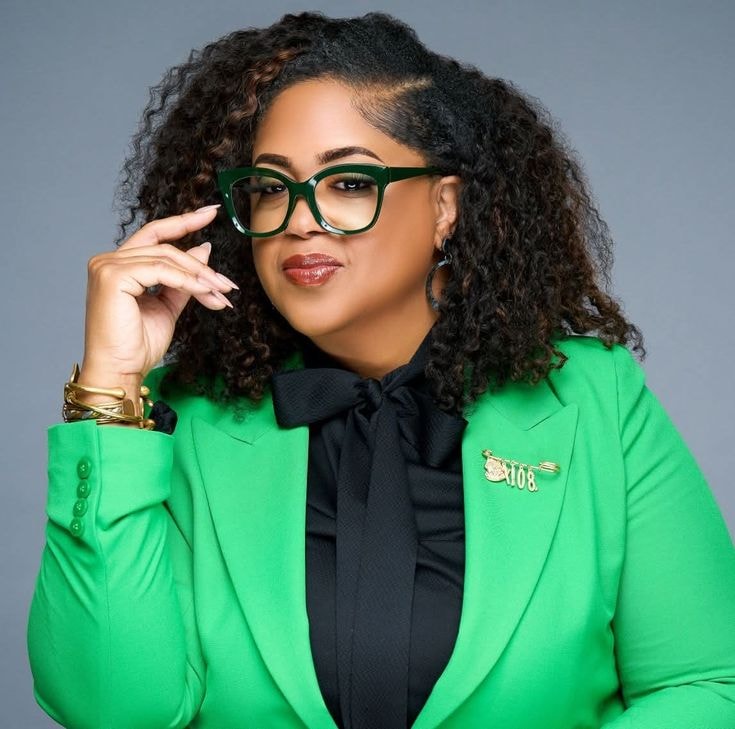 Kyra — green blazer, black bow blouse, glasses, headshot