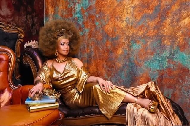 Marsha — gold metallic gown, reclining on chaise, copper teal backdrop, crown